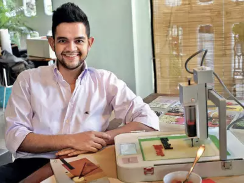 man in purple shirt sitting next to 3d food printing machine which enables eating design