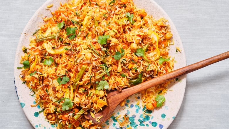 white plate with a wooden spoon digging into a vibrant yellow pile of rice and vegetables topped with chopped green coriander