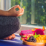 woman sitting cross legged in front of window meditating with plate of fruit next to her